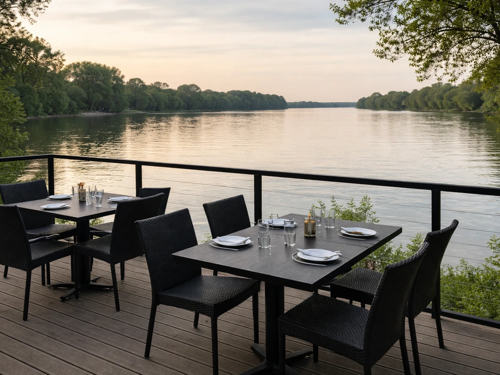 Quiet riverfront patio with tables and chairs overlooking a calm river near a restaurant.