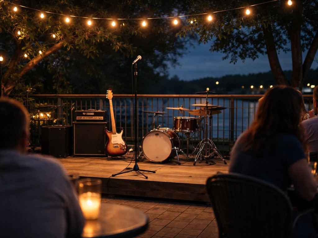 View from a patio seat toward a small outdoor stage with instruments, amps, and string lights at night.